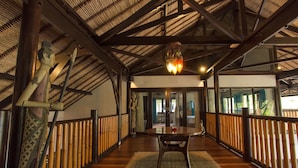 A wooden deck with a table and chairs, bamboo railings, and a ceiling with exposed beams and a hanging light fixture.