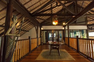 A wooden deck with a table and chairs, bamboo railings, and a ceiling with exposed beams and a hanging light fixture.