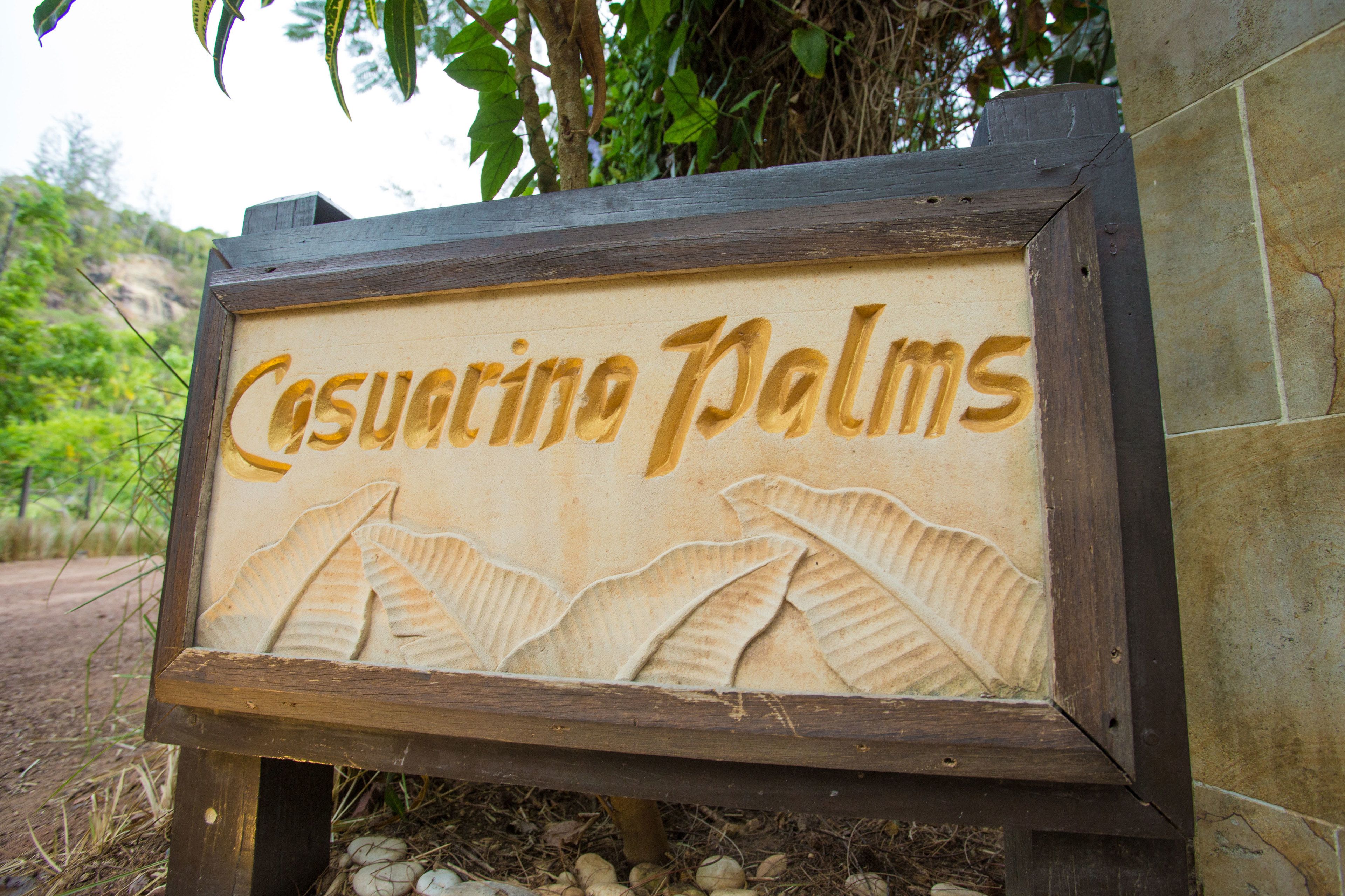 Uma placa de madeira com o texto 'Casuarina Palms' e um desenho de folha.