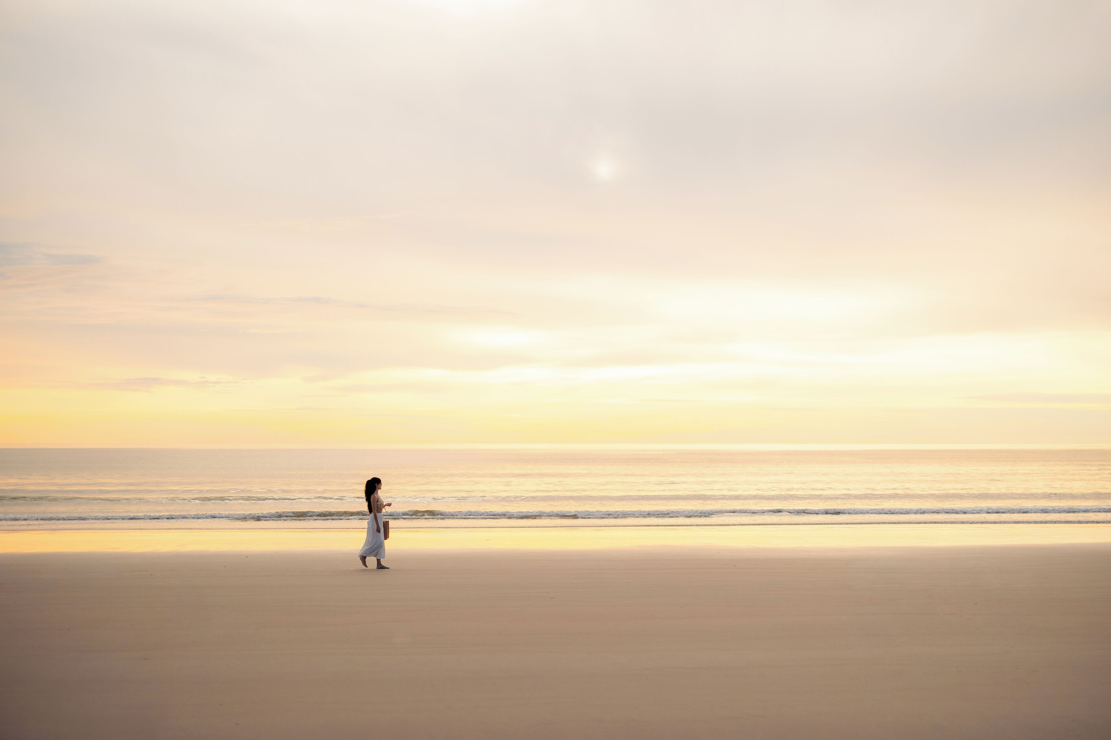 A person walking on a beach with a calm sea and a clear sky.