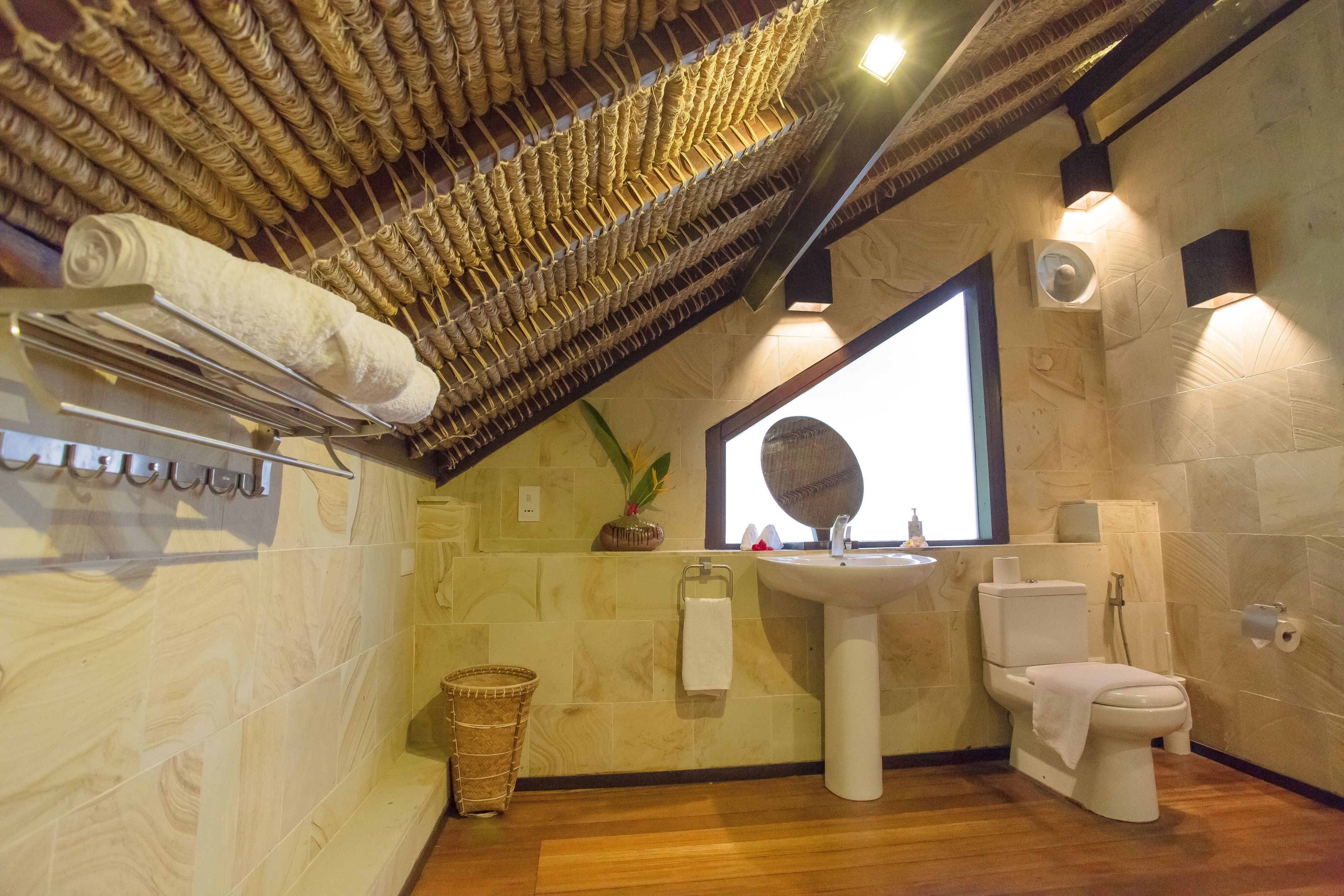 Un baño con techo de madera, un lavamanos, un inodoro y un ventanal grande.