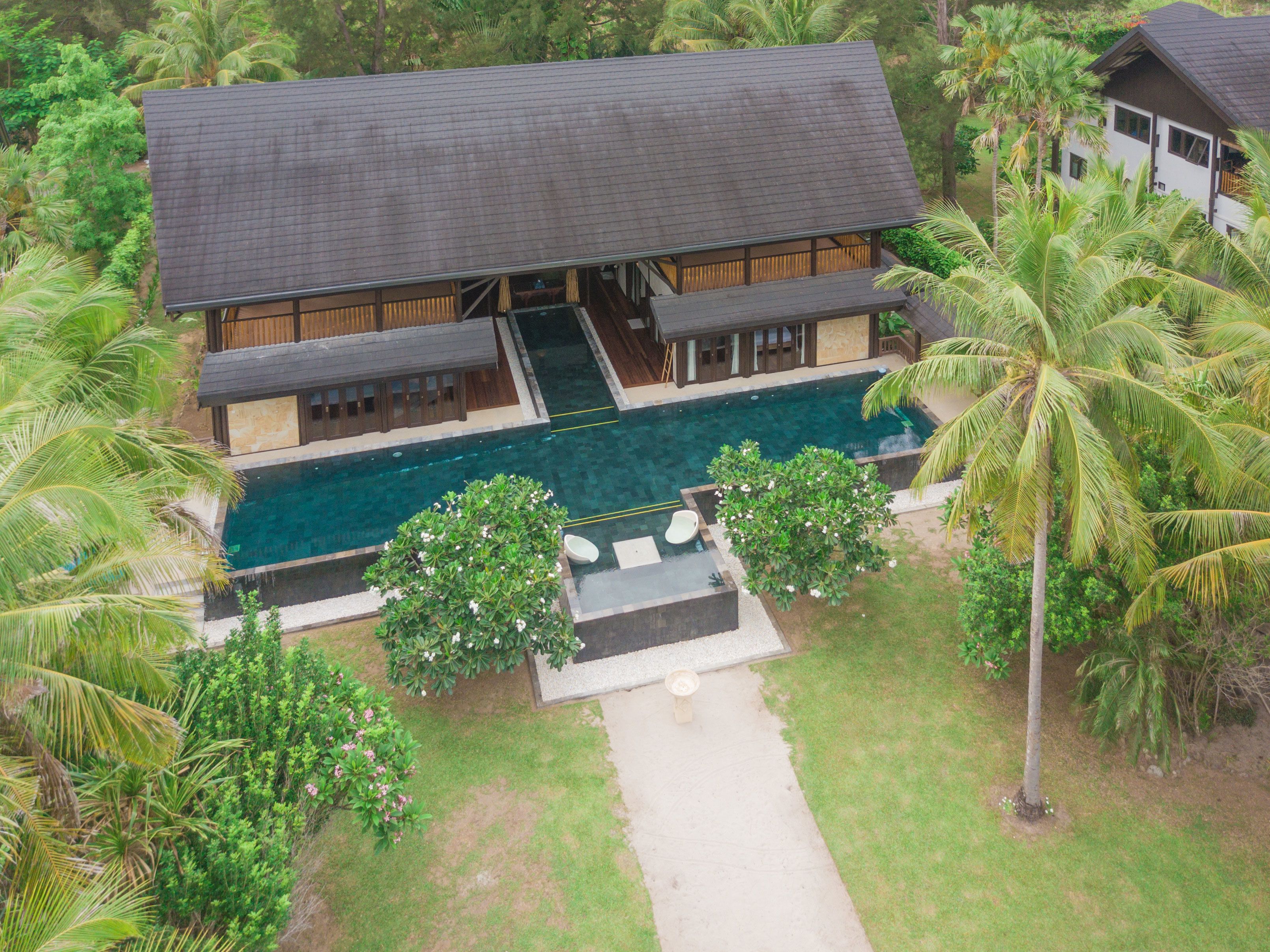 A two-story resort with a swimming pool, surrounded by palm trees and lush greenery.