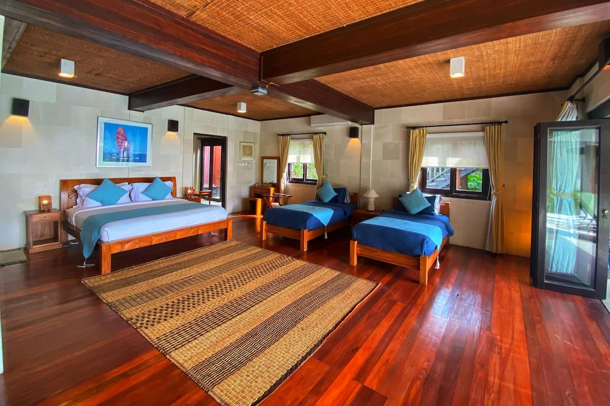 A spacious bedroom with two wooden beds, a large woven rug, and a ceiling fan.