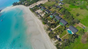 An aerial view of a coastal resort with beachfront properties, a swimming pool, and lush greenery.
