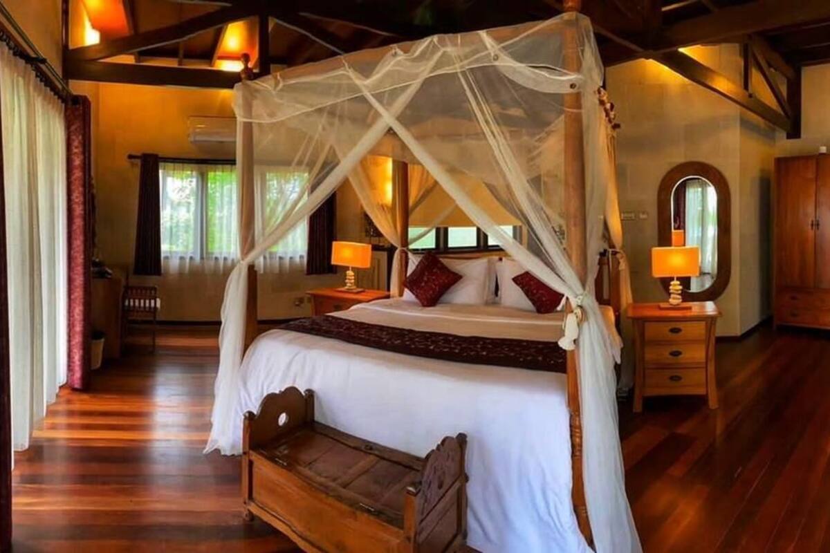 A spacious bedroom with a four-poster canopy bed, wooden furniture, and a large mirror.