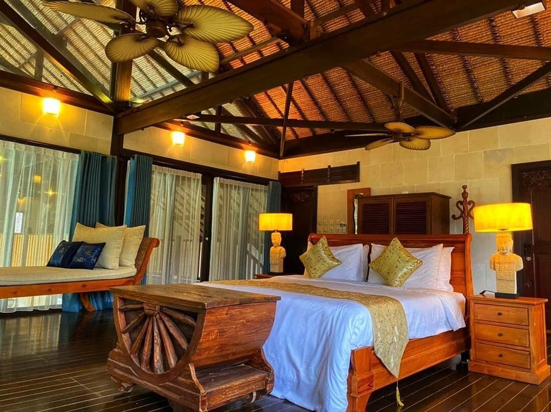 A spacious room with a large bed, a wooden bench, and a ceiling fan.