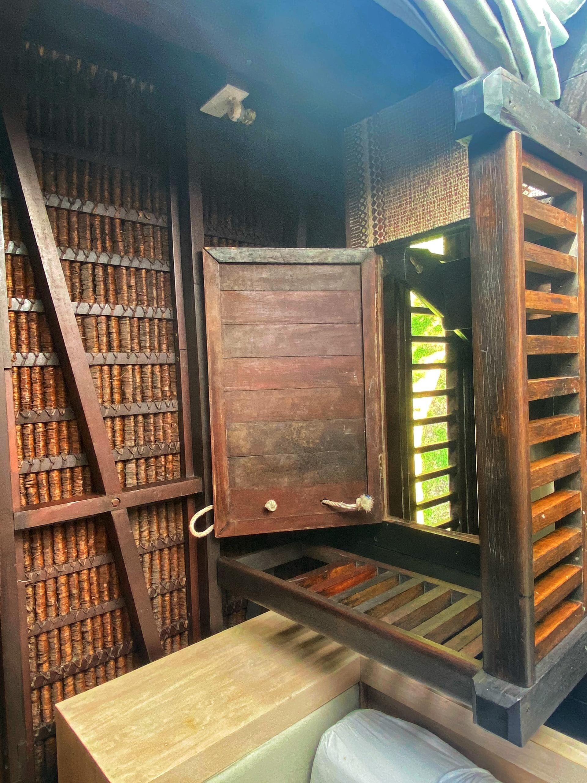 A rustic wooden structure with a sliding door, shelves with woven baskets, and a bench.