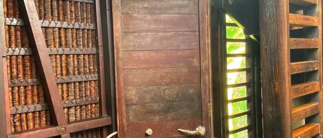 A rustic wooden structure with a sliding door, shelves with woven baskets, and a bench.