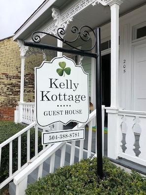 Welcome to Kelly Cottage, a charming guest house with a white porch and black sign holder.
