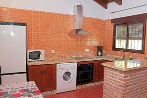 Compact kitchen area with a washing machine, microwave, and coffee maker, featuring a tiled backsplash and brick accent wall.