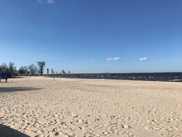 En sandstrand med fotspår, en fyr och en klarblå himmel.