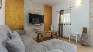 Ein Wohnzimmer mit grauem Sofa, einem Flachbildfernseher an einer Steinwand, einem kleinen Tisch, einem weißen Sessel und einer dekorativen Vase.