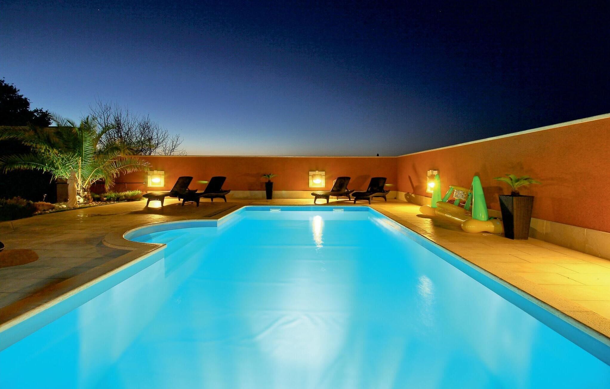 A swimming pool with lounge chairs and potted plants, surrounded by a low wall and palm trees.