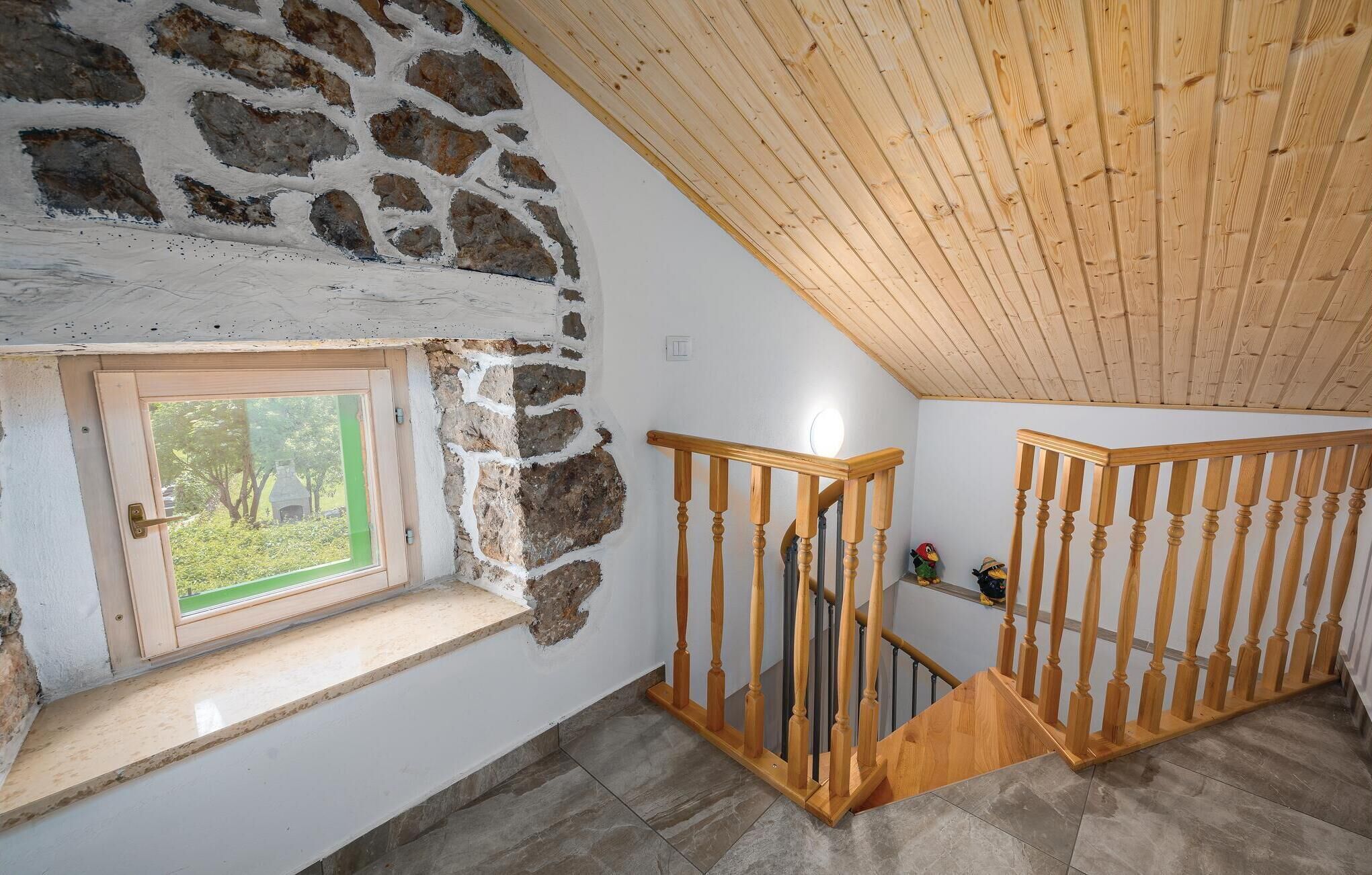 Une pièce avec un mur en pierre, un escalier en bois et une fenêtre donnant sur un paysage verdoyant.
