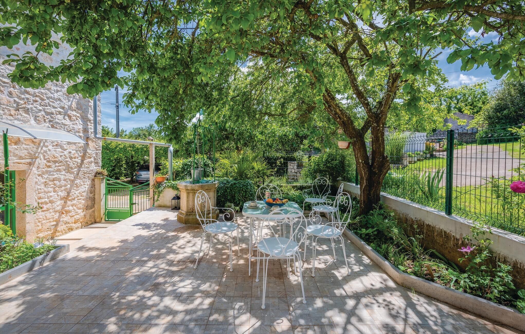 Un patio al aire libre con un muro de piedra, una valla metálica y un árbol que da sombra.