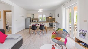 Un espacio habitable compacto con kitchenette, comedor y una pequeña zona de estar con una silla colorida.