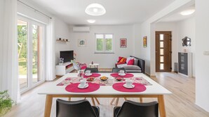 Amplia sala de estar con una mesa de comedor preparada para dos personas, un sofá, un televisor y una puerta que da a otra habitación.