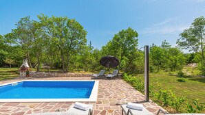 Una piscina con baldosas de piedra, sillas de descanso y una parrilla.