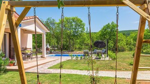 Un conjunto de columpios de madera con dos columpios rojos, una piscina y un patio con mobiliario exterior.