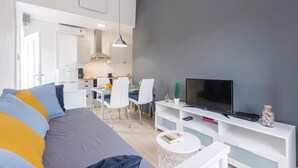 Un soggiorno moderno con un divano, una TV su un mobile bianco e una zona pranzo con sedie e tavolo.