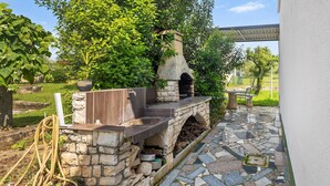 Un horno de pizza de piedra con chimenea, rodeado por un muro de piedra y un patio con mosaicos.