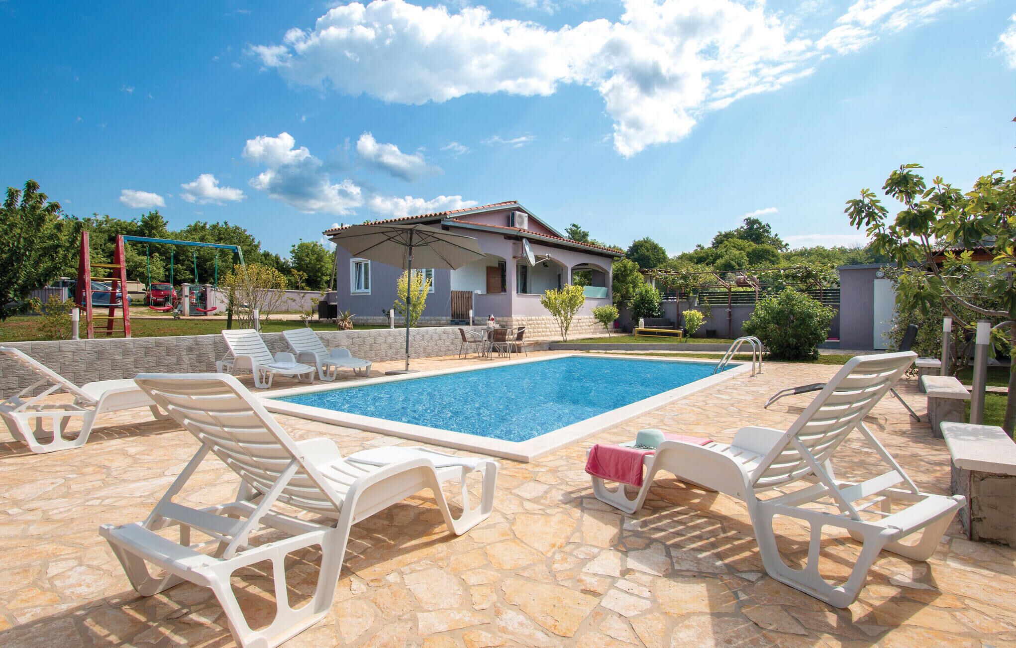 A swimming pool with lounge chairs, a covered patio, and a house in the background.