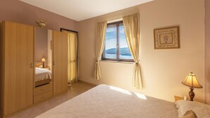 Quarto com cama, guarda-roupa, janela com cortinas, abajur e um quadro na parede.