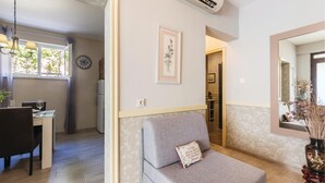 Uma sala de estar aconchegante com um sofá, uma mesa de jantar com cadeiras, um relógio e um quadro na parede.