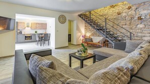 A modern living room with a stone wall, a staircase, and a kitchen in the background. - Awesome home in Peruski with WiFi (Peruski)