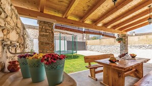 An outdoor patio with a wooden table and benches, a stone pillar, and a green trampoline in the background. - Awesome home in Peruski with WiFi (Peruski)