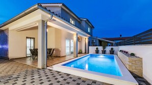 Une maison moderne dotée d’une piscine, d’un patio couvert et d’un espace salon extérieur.