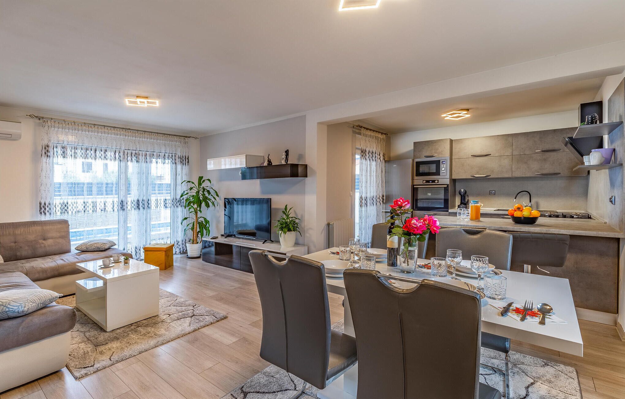 Un appartement moderne comprenant un coin repas, une cuisine, un salon et un balcon agrémenté de rideaux.