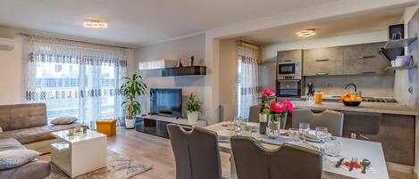 A modern apartment with a dining area, kitchen, living room, and a balcony with curtains.