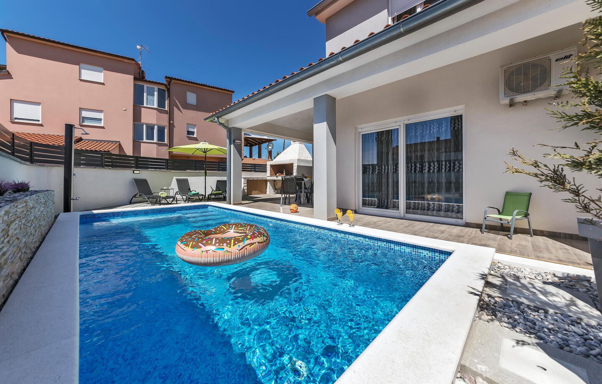 A swimming pool with a donut float, lounge chairs, and a covered patio area.