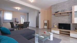 A modern living room with a sofa, a glass coffee table, a TV, and a stone wall. - Stunning home in Vodnjan (Vodnjan)