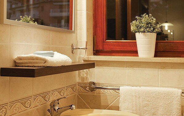 A bathroom with a white sink, a towel rack, a window with a plant, and a wooden shelf with towels.