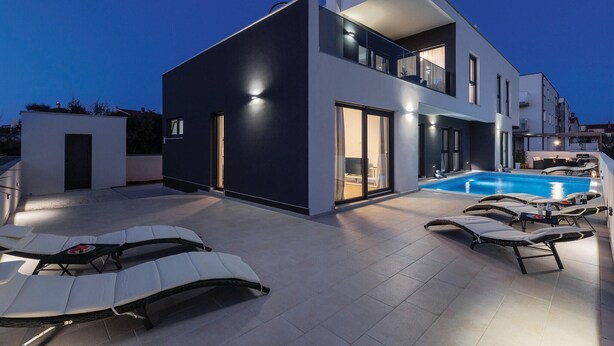 A modern two-story house with a swimming pool, outdoor seating, and a well-lit balcony. - Luxurious home in Pula (Pula)