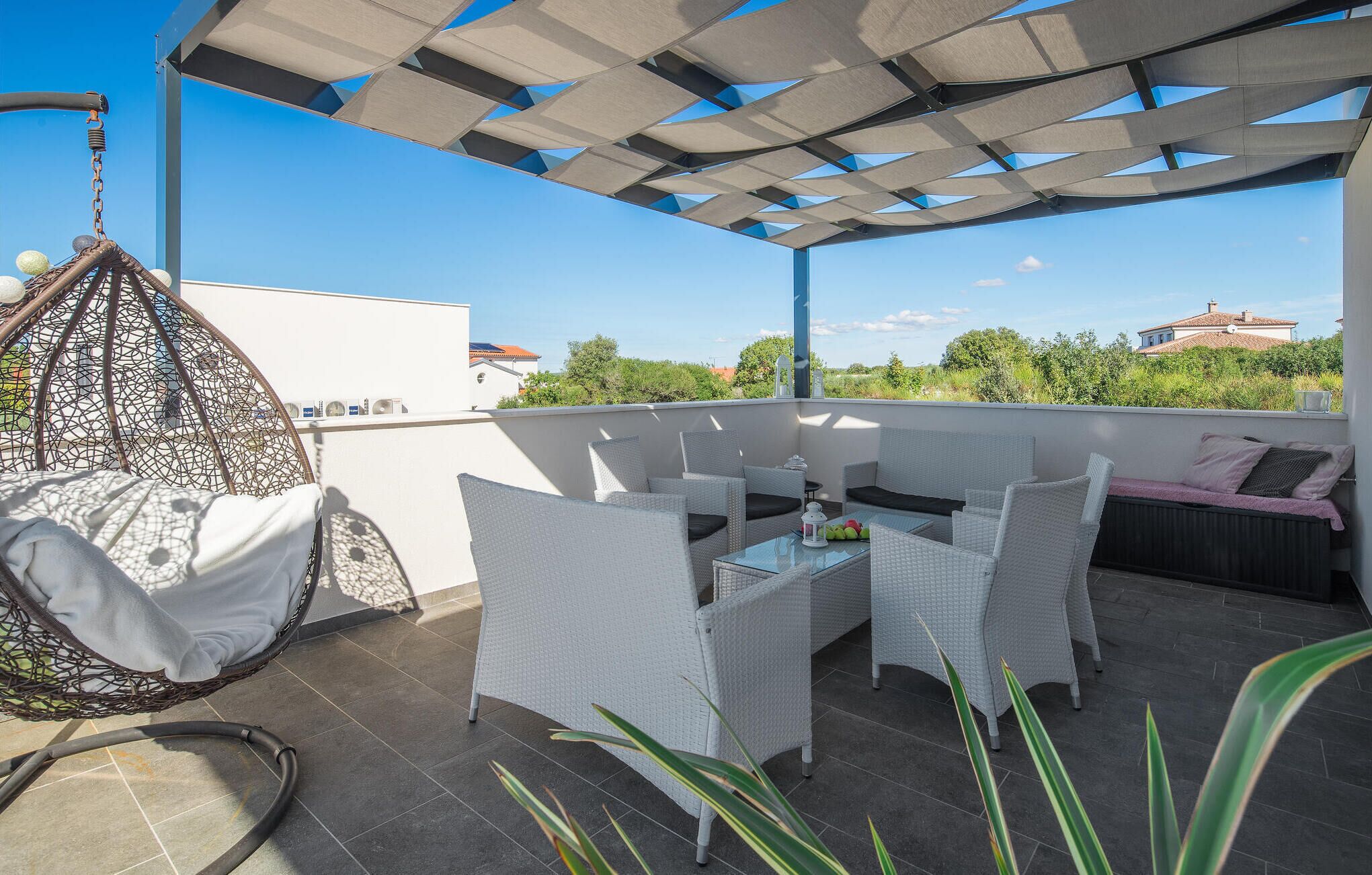 A rooftop terrace with a hanging chair, a table with chairs, and a view of the surrounding area.