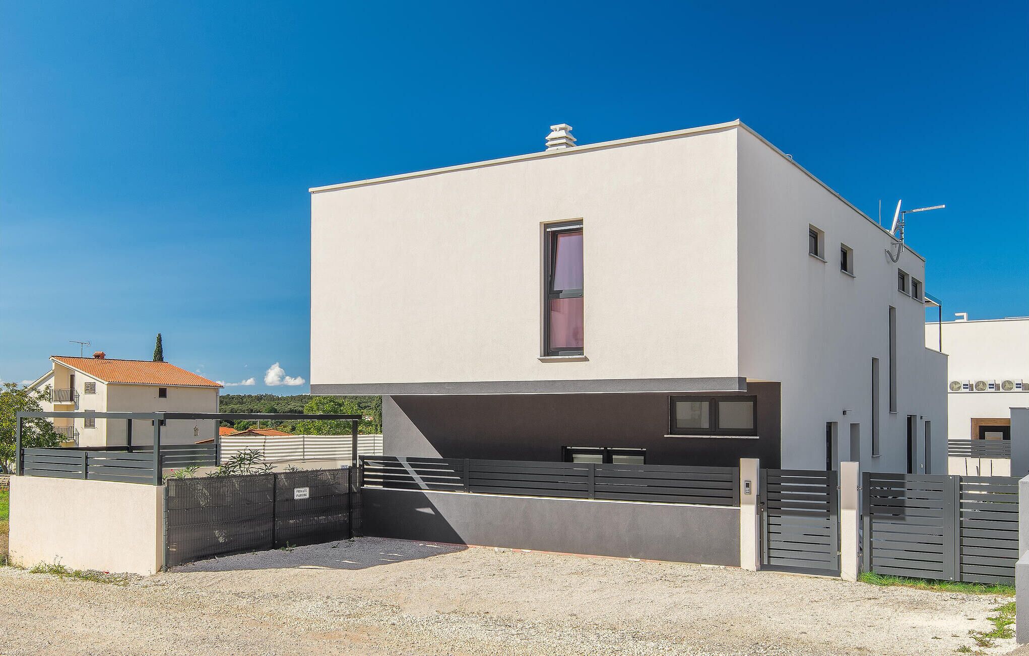 A modern two-story building with a flat roof, a central window, and a gated entrance.