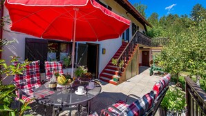 Une terrasse avec un parasol rouge, des sièges d’extérieur et un escalier menant à un deuxième étage.