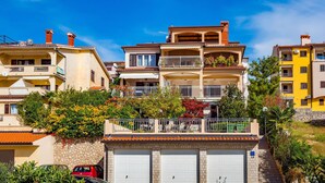 A multi-story residential building with balconies, a garage, and a staircase leading to the entrance. - Nice apartment in Rabac with house sea view (Rabac)