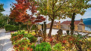 A garden with various plants and sculptures, a paved walkway, and a building with a red-tiled roof in the background. - Nice apartment in Rabac with house sea view (Rabac)