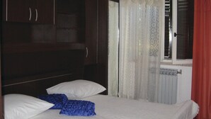 A bedroom with a bed, two pillows, a window with curtains, and a radiator. - Nice apartment in Rabac with house sea view (Rabac)