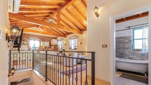 Amplia sala de estar con techo de madera alto, una cocina con paredes de ladrillo y vistas a un baño con bañera.