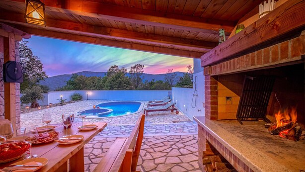 Un patio con piso de piedra, piscina, sillas de descanso y chimenea.