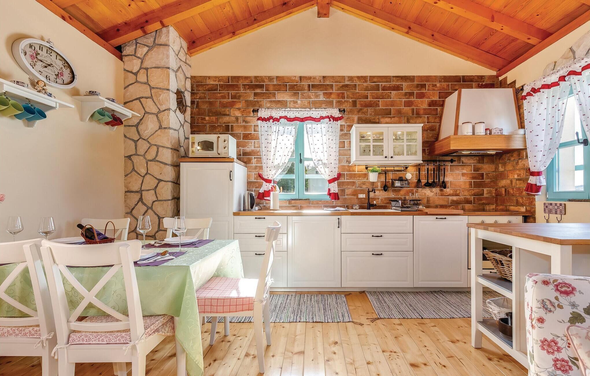 A cozy kitchen with white cabinets, a stone wall, and a wooden ceiling.