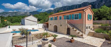 A villa with a swimming pool, outdoor seating, and a view of mountains.