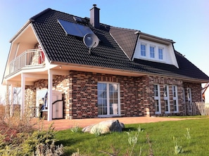 Uma casa de dois andares com fachada de tijolos, uma varanda e painéis solares no telhado.