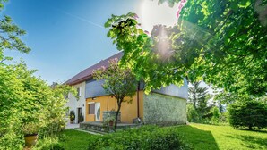 Een twee verdiepingen tellend huis met een gevel van natuursteen en een pannendak, omgeven door weelderige begroeiing en een verzorgd gazon.