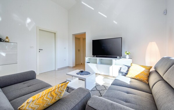 A modern living room with grey sofas, a flat-screen TV, and a white entertainment unit.